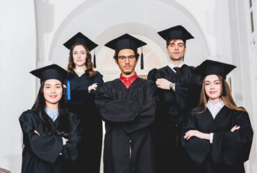 cheerful students in graduation gowns standing with crossed arms in university